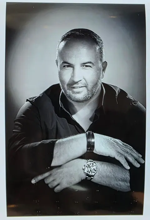 Portrait en noir et blanc d’Alexandre, bras croisés, souriant