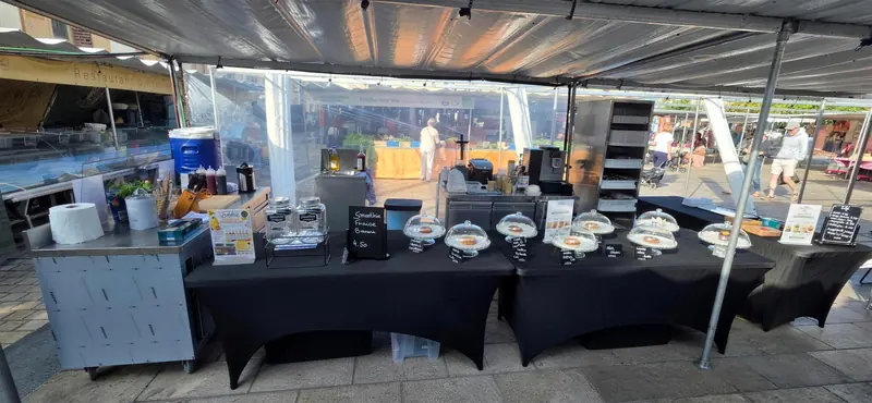 Stand de marché sous une tente, tables nappées de noir et cloches à pâtisseries