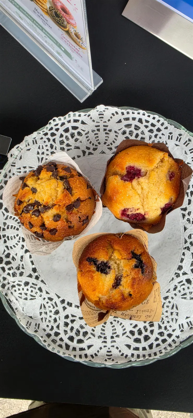 Trois muffins posés sur une dentelle blanche, dont un aux pépites de chocolat et deux aux fruits rouges