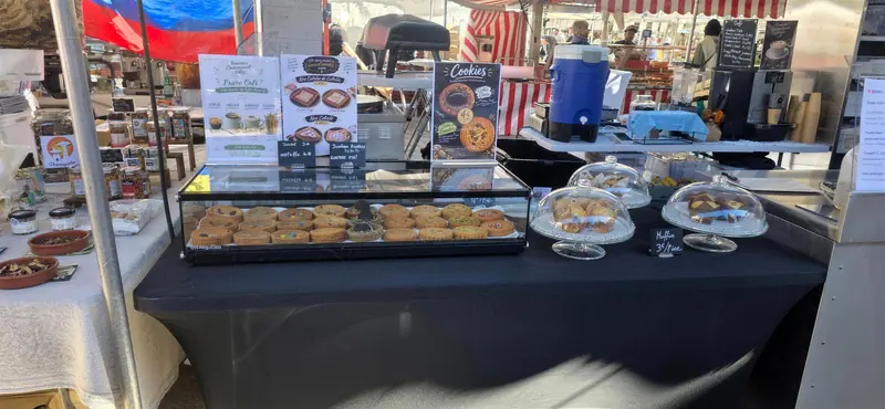 Stand de jour au marché, avec une vitrine de cookies et des cloches de pâtisseries